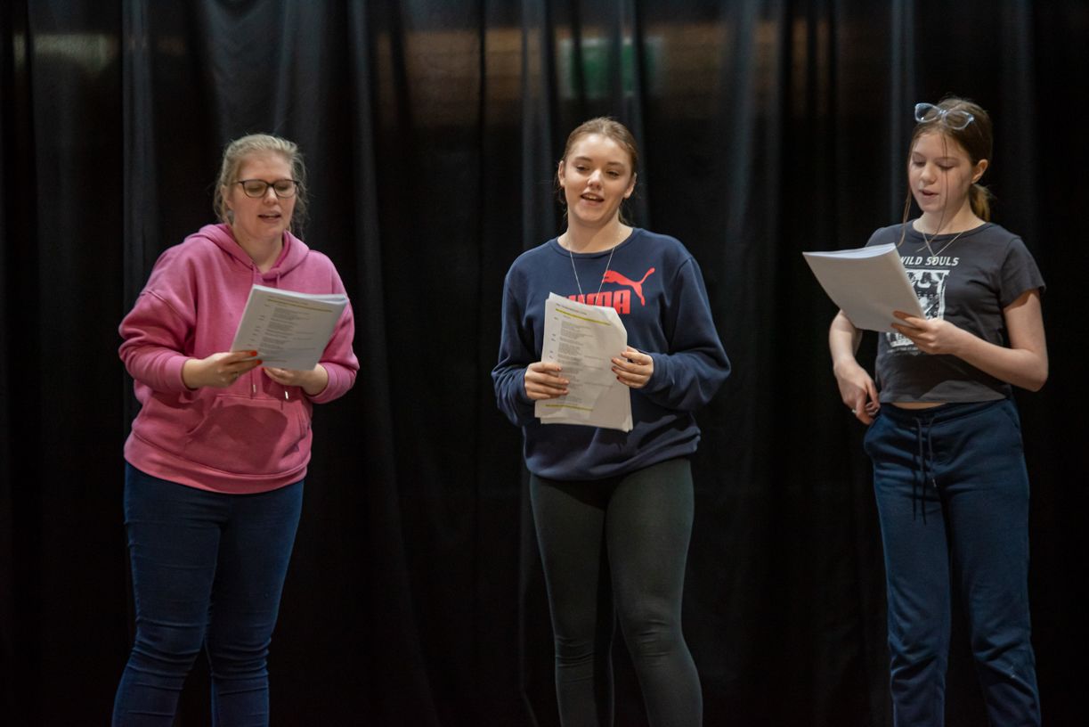 Three young women are standing on a stage holding papers.