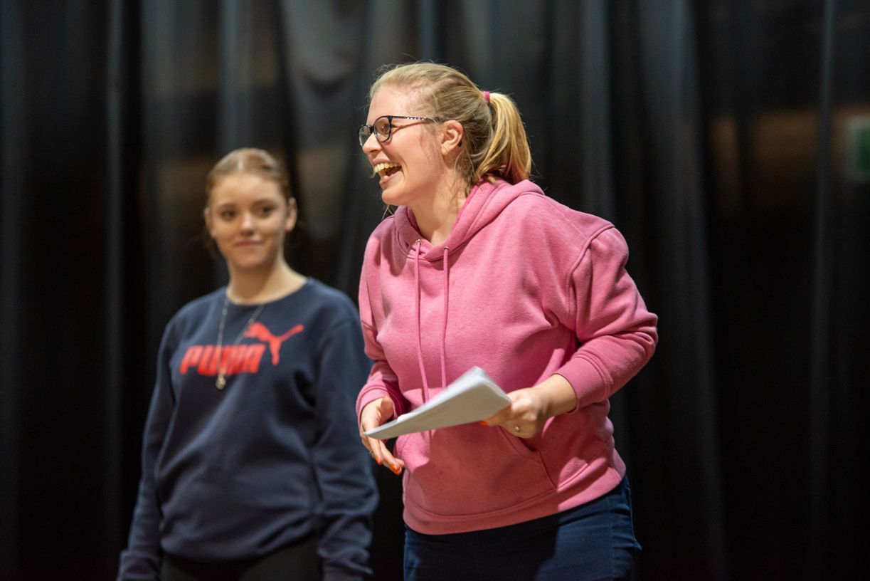 A woman in a pink hoodie is laughing while holding a piece of paper.