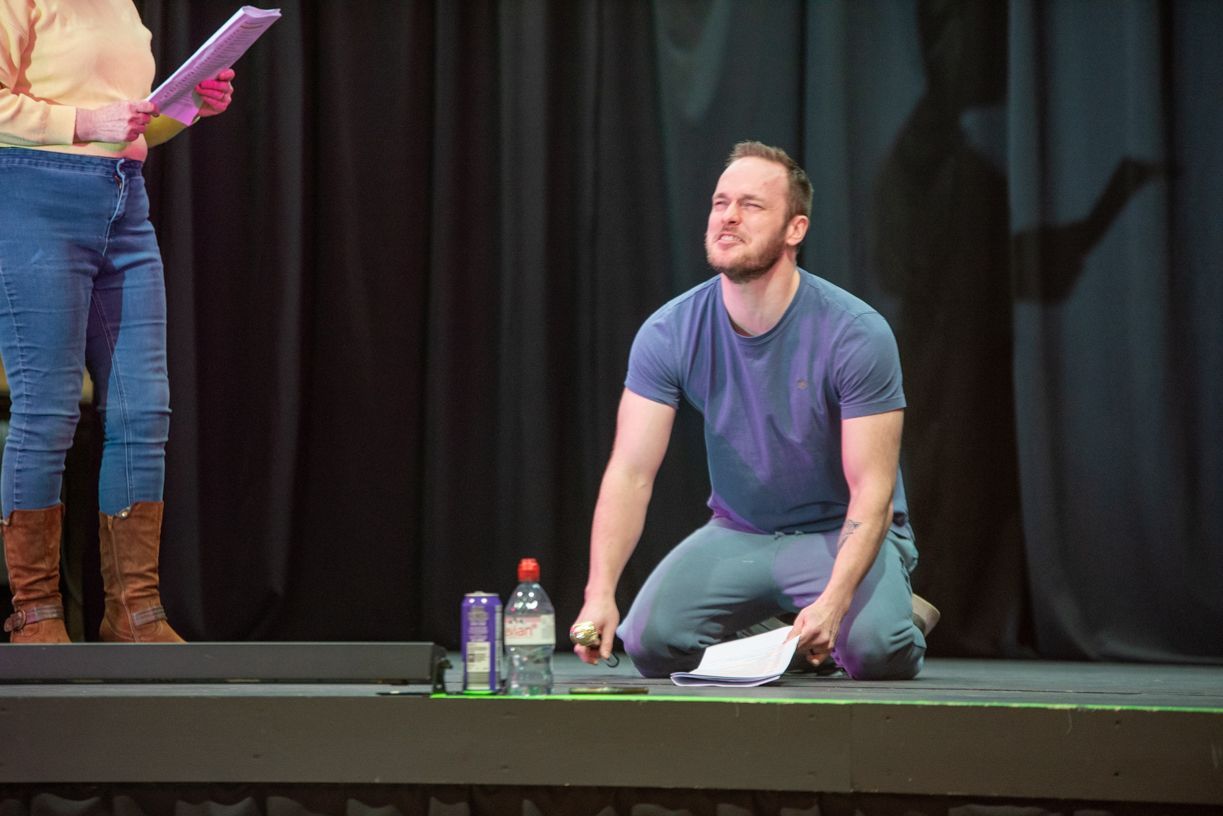 A man is kneeling on a stage with a woman standing behind him.