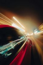 Blurred night street scene with colorful light trails reflected on a car