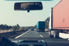 View through a car windshield of trucks driving on a highway, including a red trailer and blue container truck.