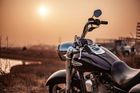 Black motorcycle at sunset on a rural road, with warm orange sky and sun low on the horizon