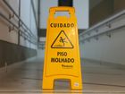 Yellow wet floor warning sign in a hallway, marked “Cuidado Piso Molhado.”