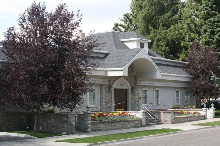 A white building with a gray roof is surrounded by trees