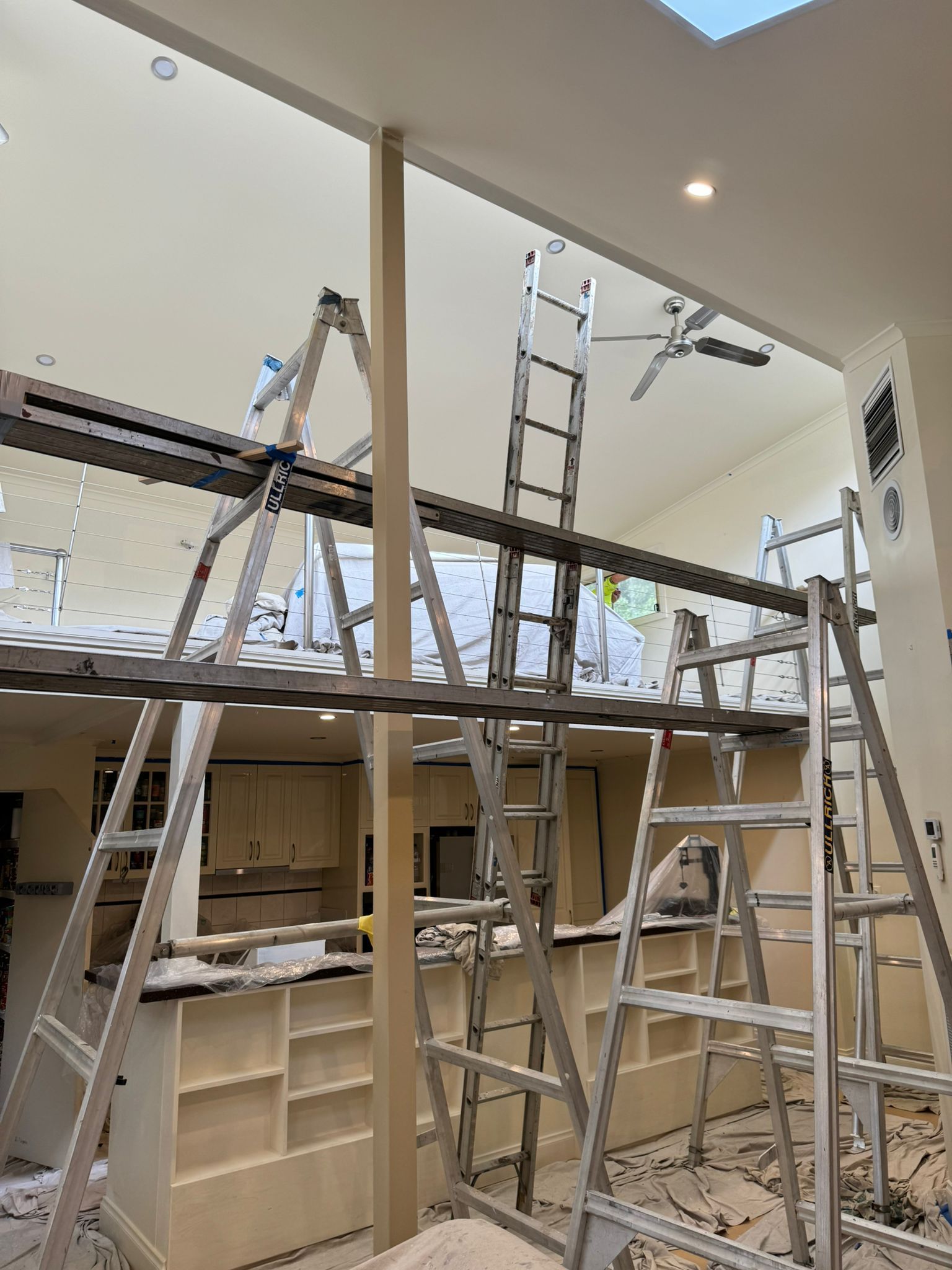 Interior view of a kitchen under construction with multiple ladders and scaffolding for high ceiling work — Andrew Harper Painting & Decorating in Albury, NSW