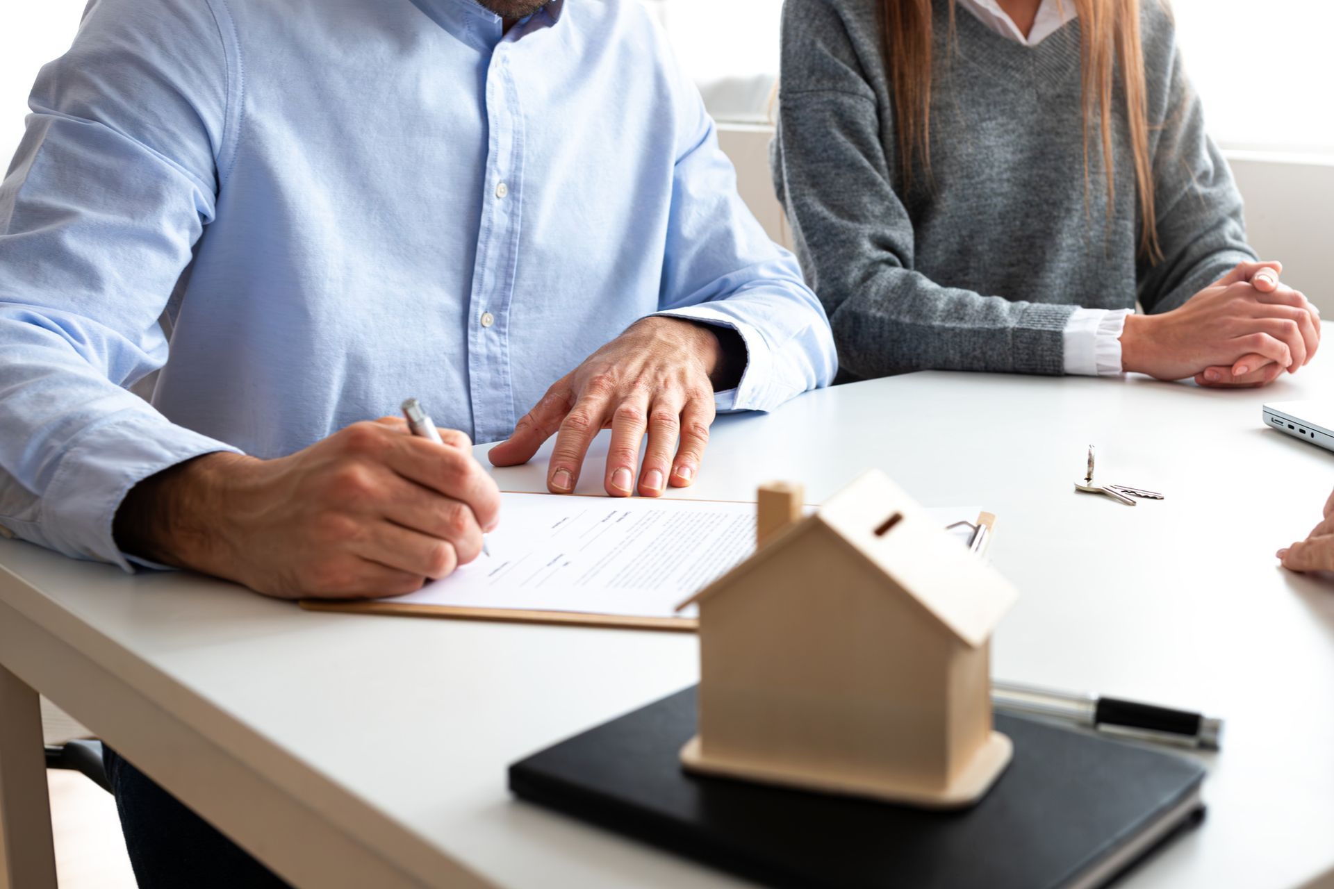 A man is signing a new home purchase agreement next to his wife.