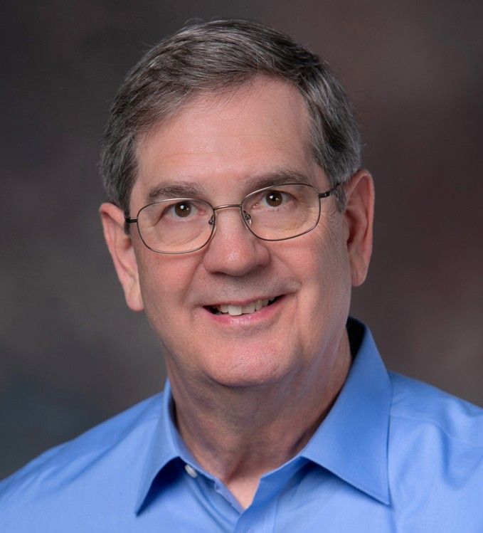 Smiling man in a light gray shirt against a neutral gray background