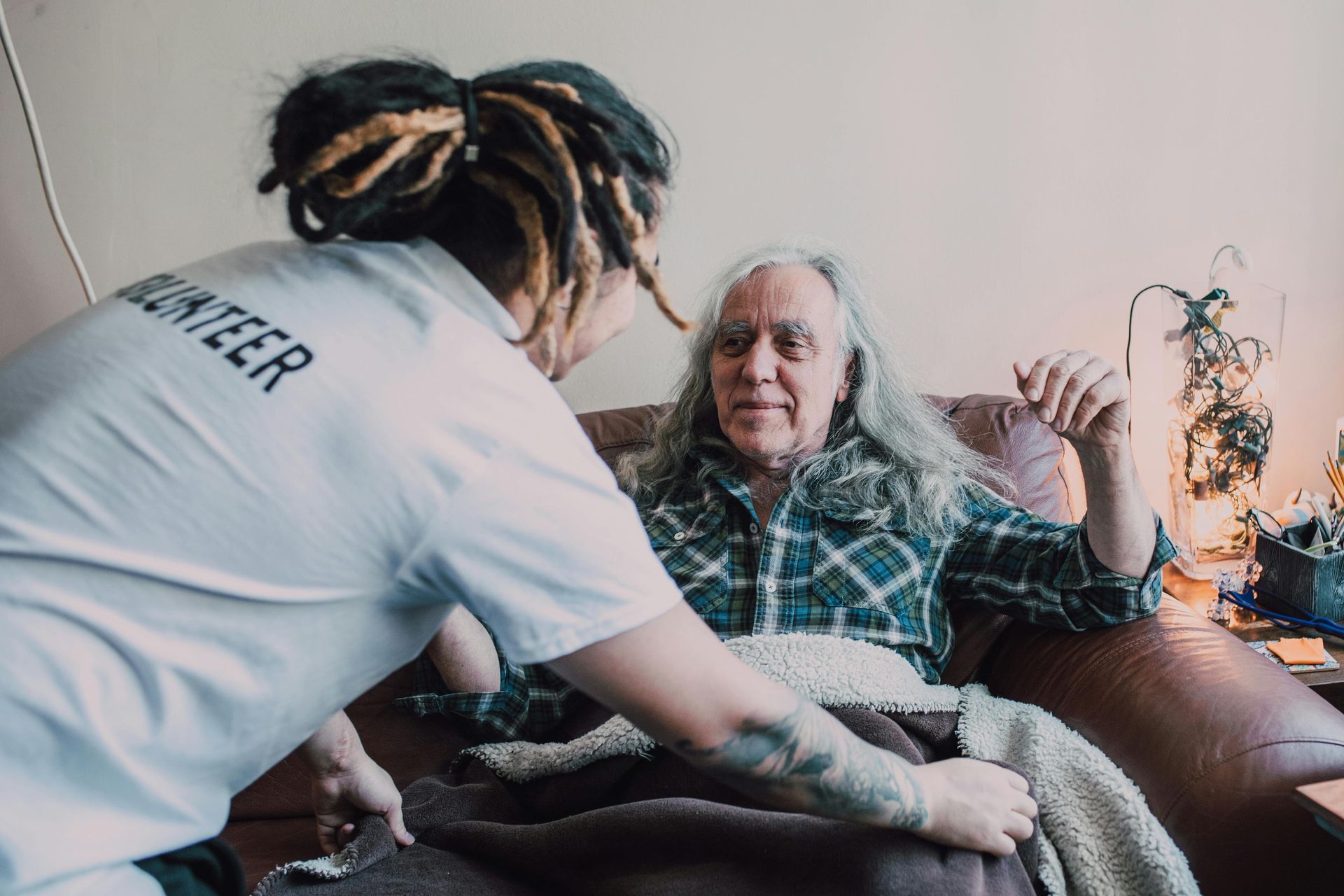 Caregiver tending to an elderly person on a couch in a cozy living room