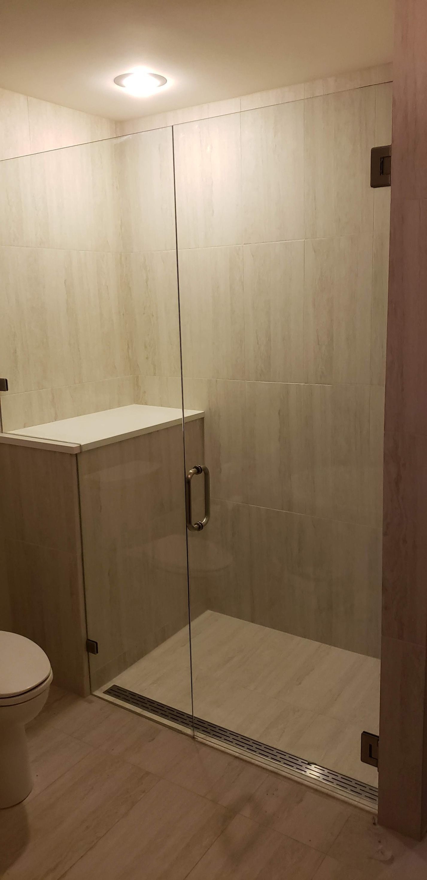 A modern bathroom featuring a glass shower enclosure with a built-in bench and a toilet.