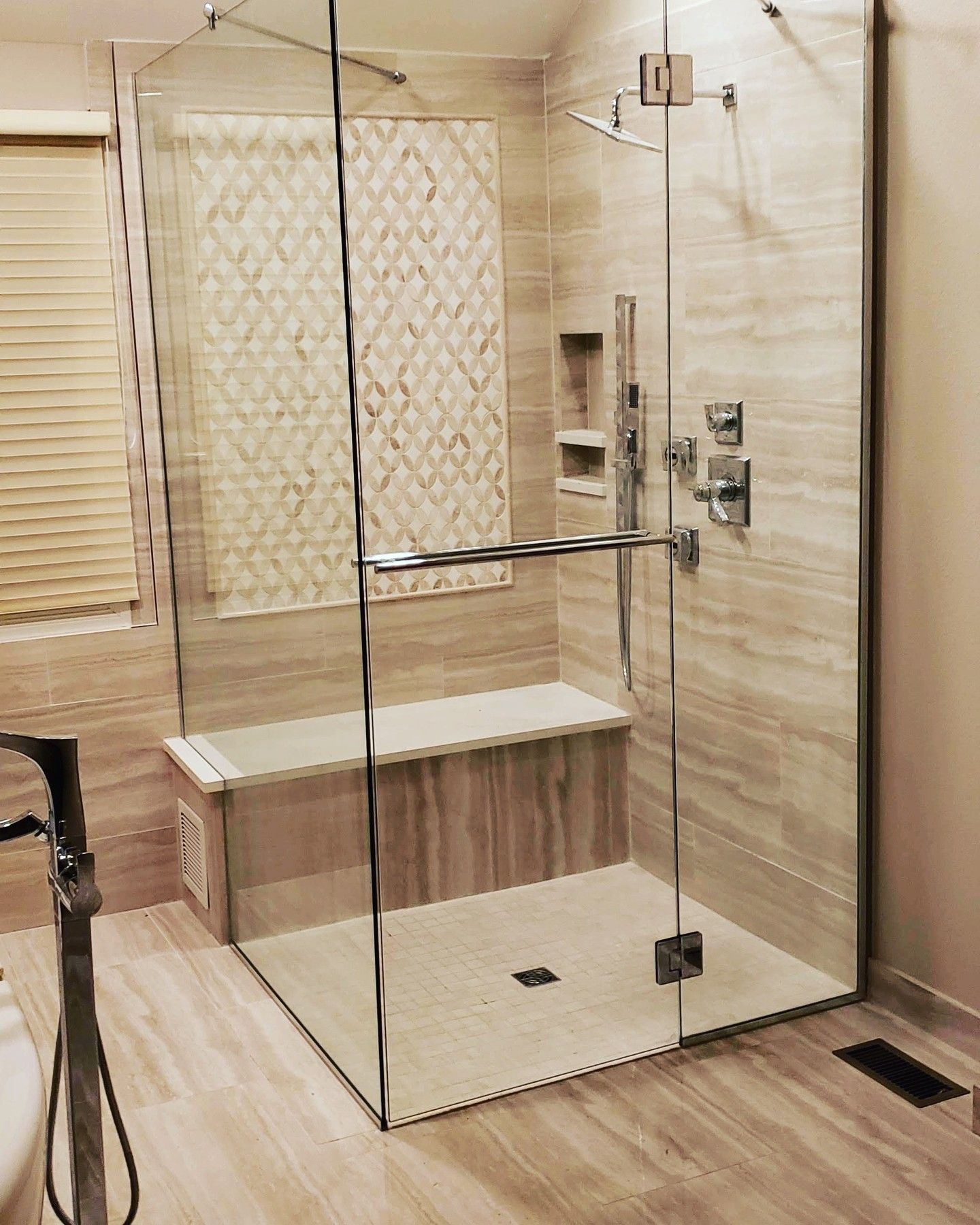 A modern bathroom with a glass-enclosed shower, a built-in bench, and light-colored tile flooring and walls.