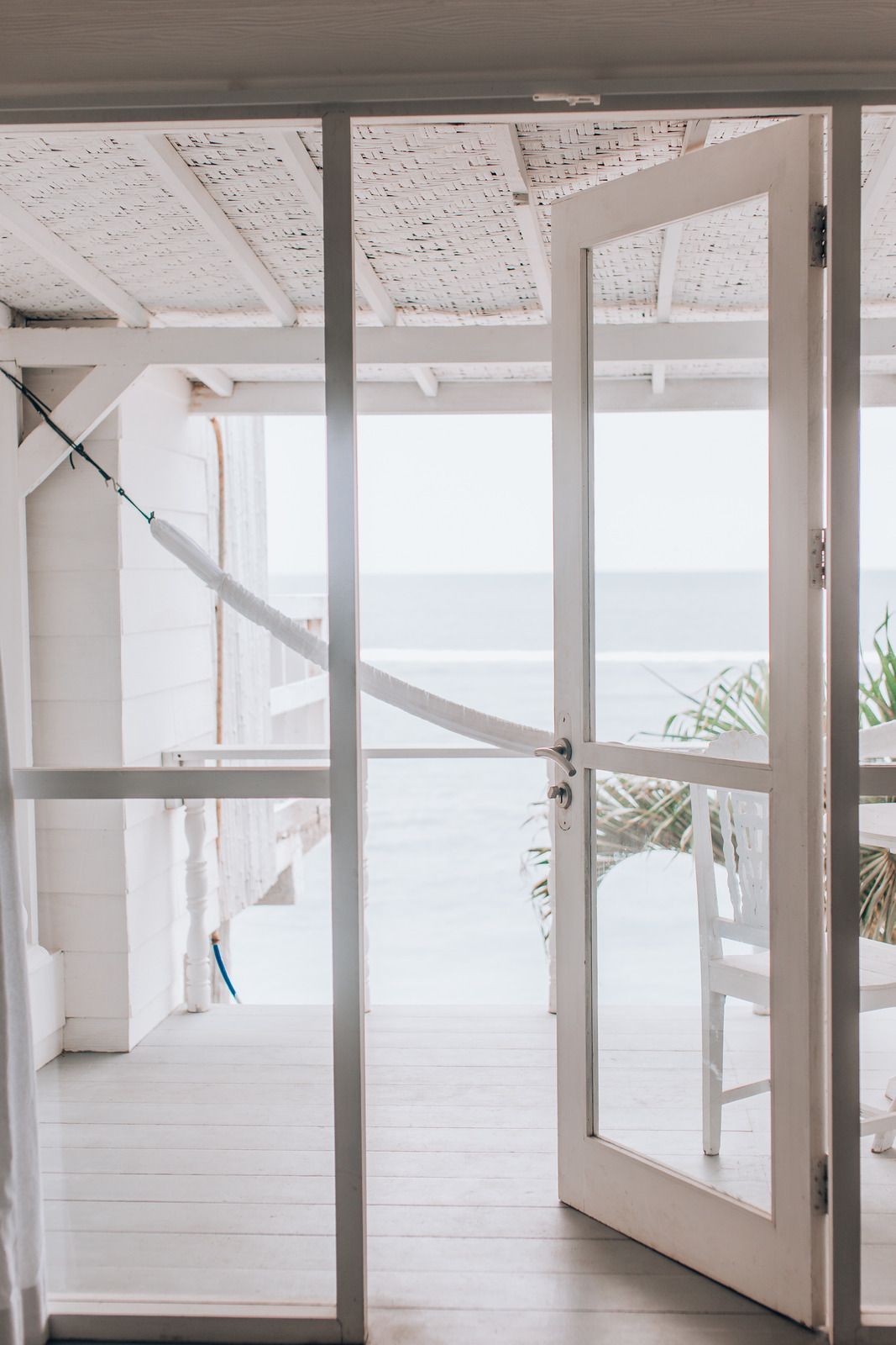 White porch with open door overlooking the ocean, featuring a hammock and furniture.