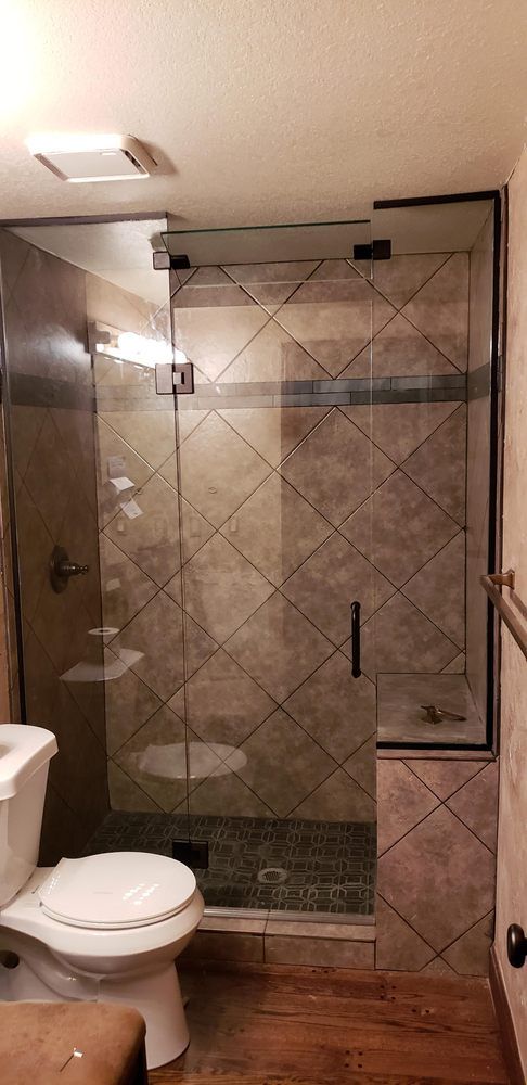 A modern bathroom with a glass shower enclosure, toilet, and wood flooring.