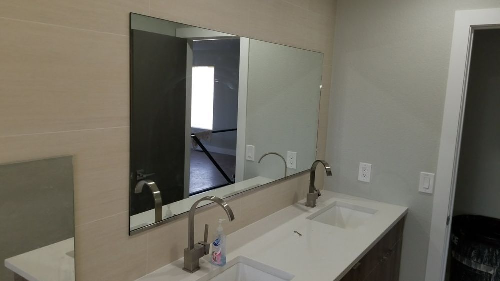 A modern bathroom with a double sink and large mirror reflecting a doorway and room. Gray walls and a light countertop.