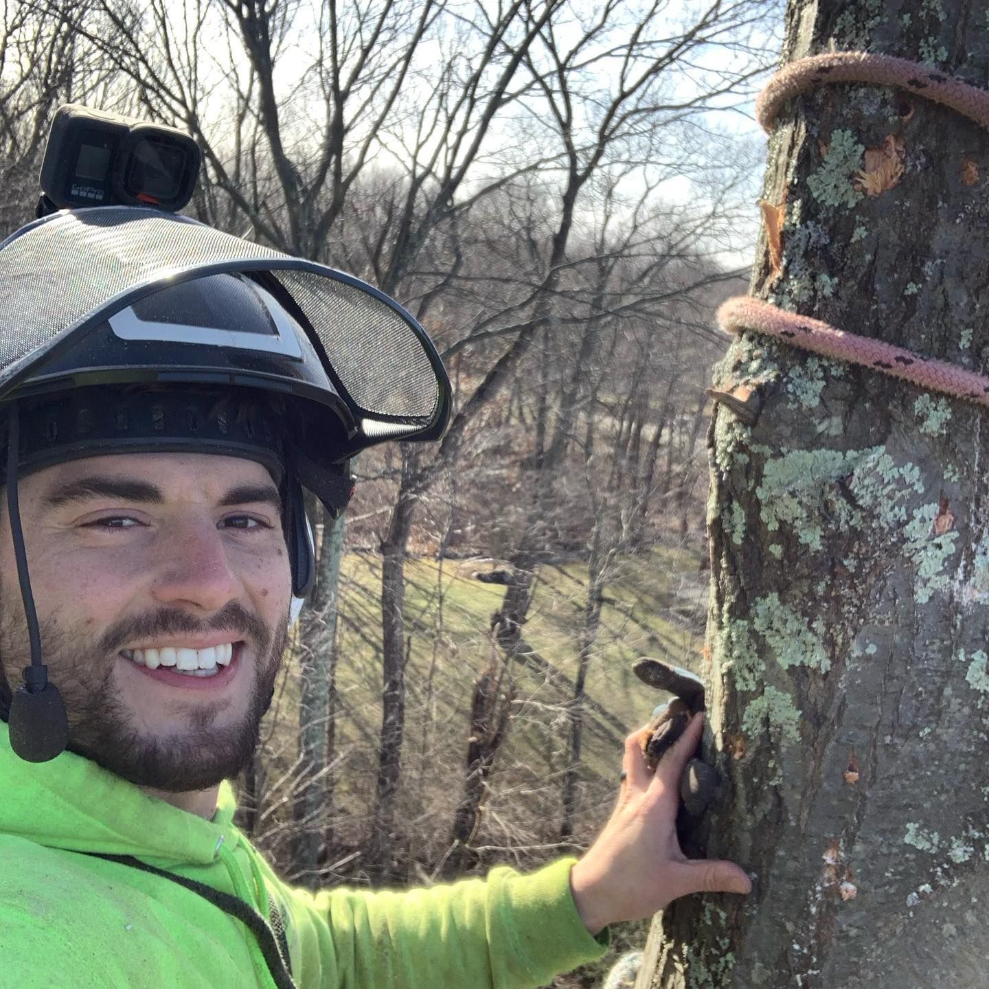 A man wearing a helmet and a green shirt is standing next to a tree.