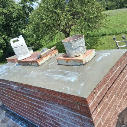 Brick chimney top with two metal cans and a white jug on bricks against green trees