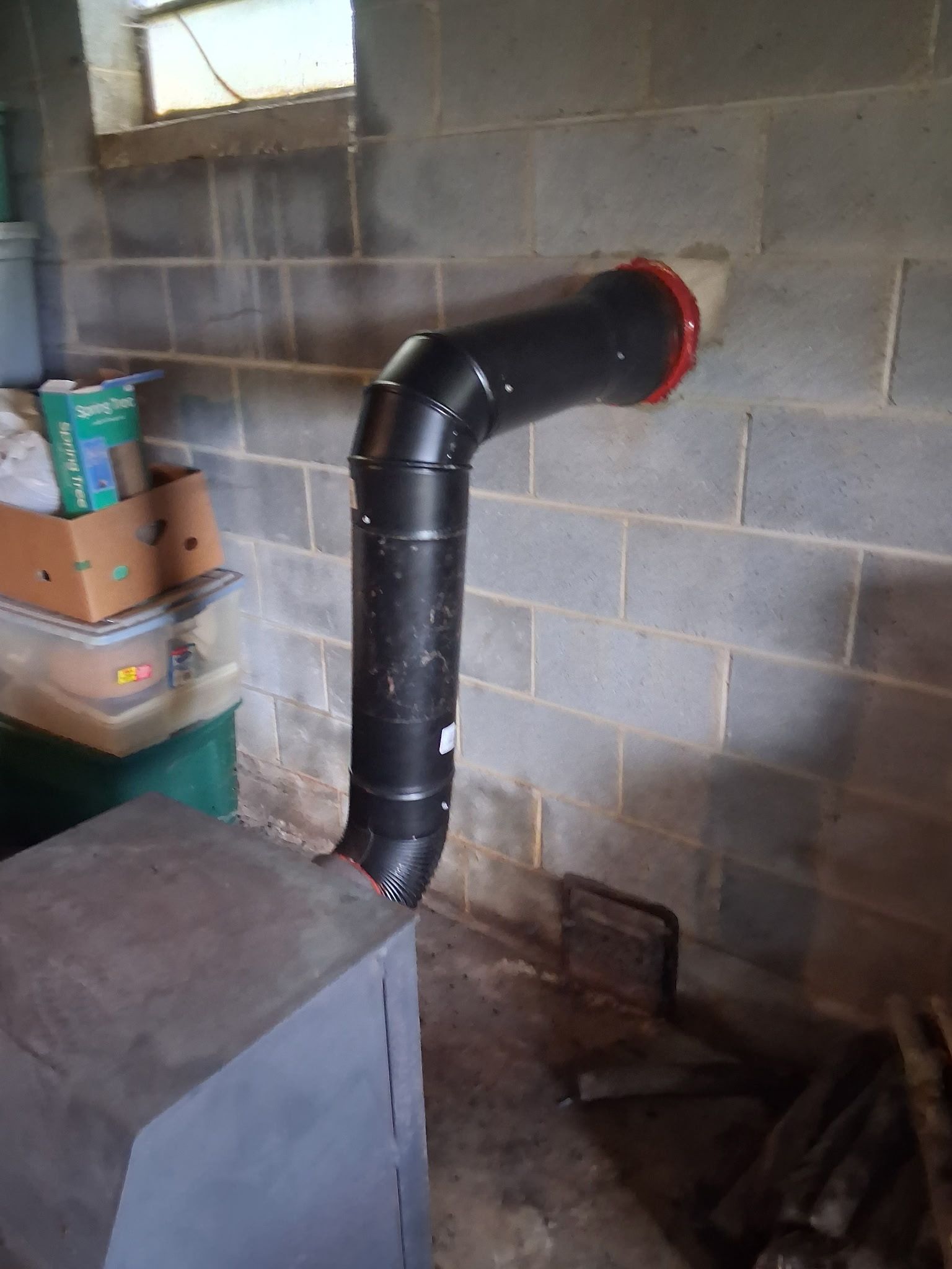 Black insulated pipe elbow venting through a cinder block wall in a basement room