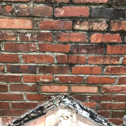 Red brick wall with a small triangular roof peak at the bottom edge, showing weathered mortar and bricks