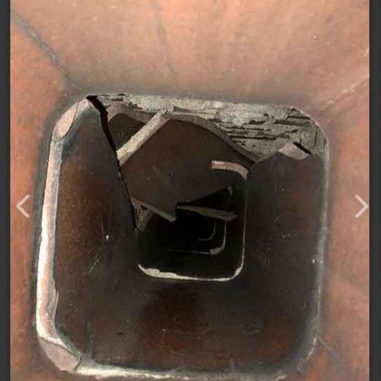 Inside a square metal duct or pipe, showing a dark, damaged interior with peeling edges and debris.