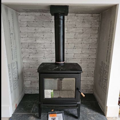 Black wood-burning stove with chimney in a small white alcove against a brick wall.