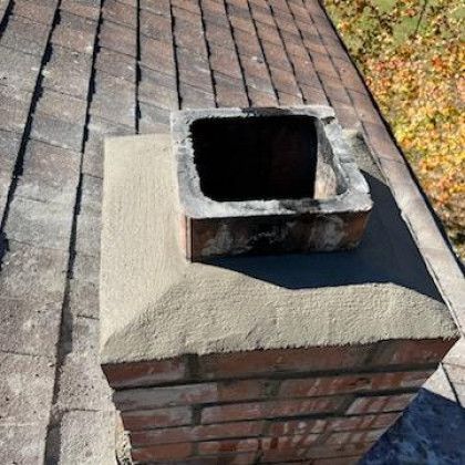 Brick chimney with a square metal flue on a shingled roof, viewed from above.