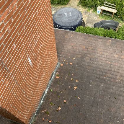 Brick wall beside a shingled roof with a black trash bin and bench in a small yard
