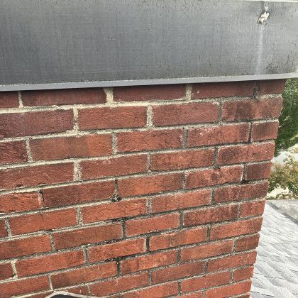 Red brick wall below gray siding with visible mortar and a few chipped bricks