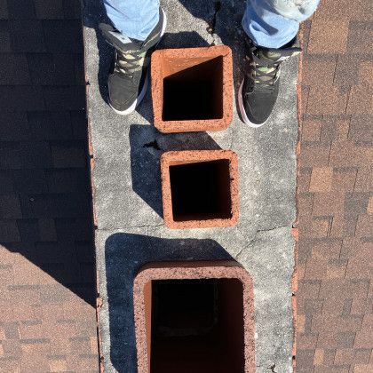 Person standing by three brick chimney flues on a rooftop, viewed from above