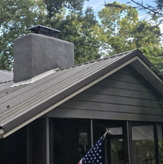 Gray chimney and metal roof on a house with trees in the background
