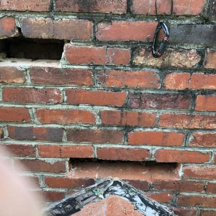 Red brick wall with two horizontal openings and a small black cable hanging near the top right.