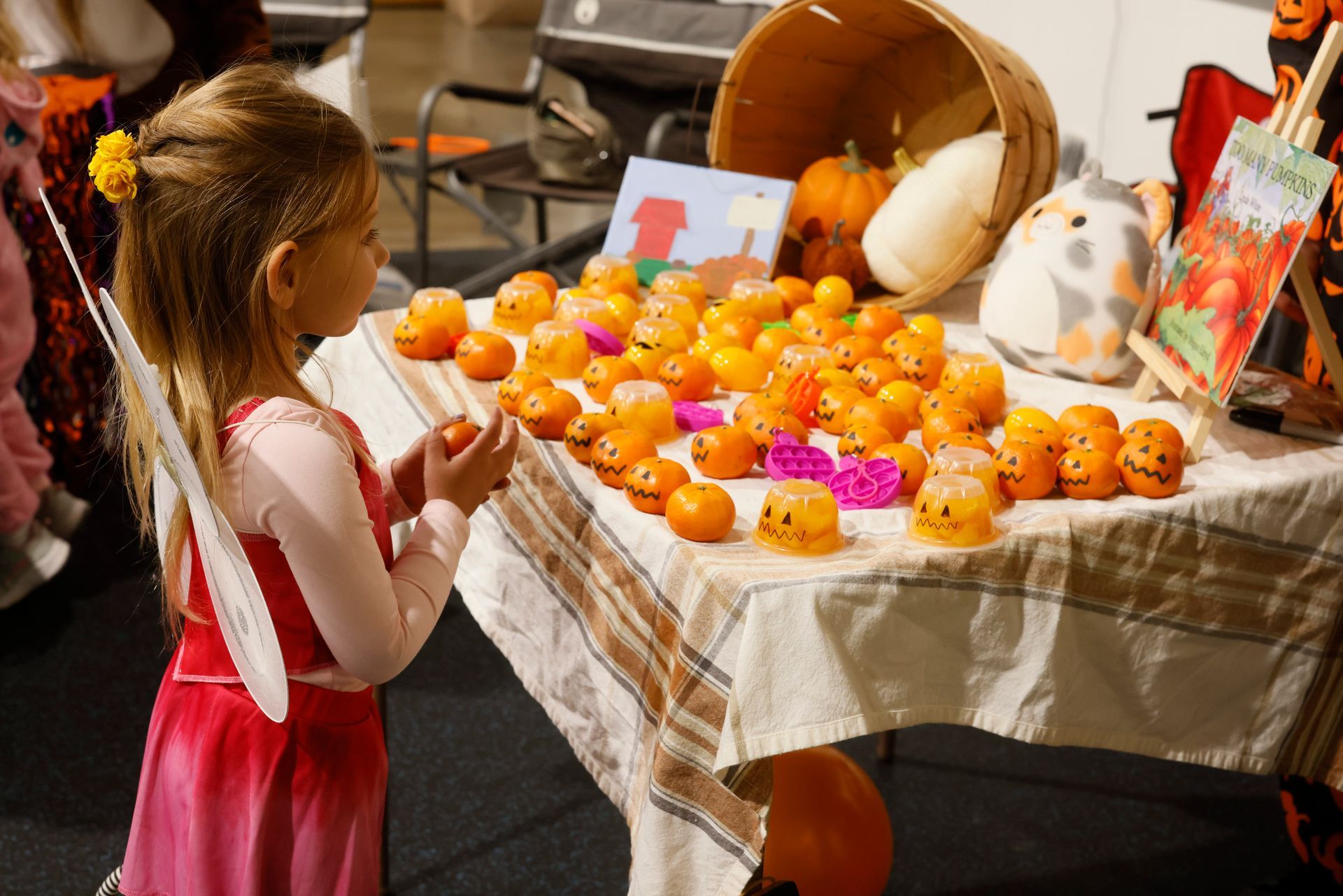 Person looking at a table filled with orange fruit and colorful decorations at a Halloween event