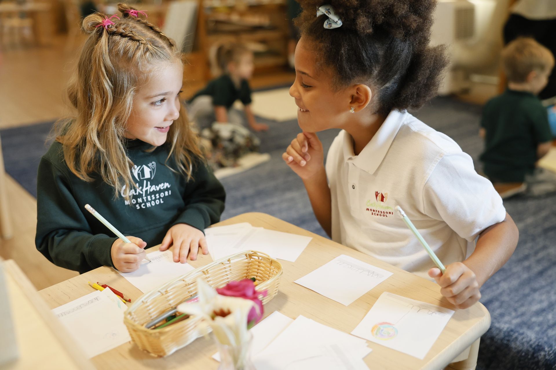 Two children working together at a table with papers and art supplies in a classroom