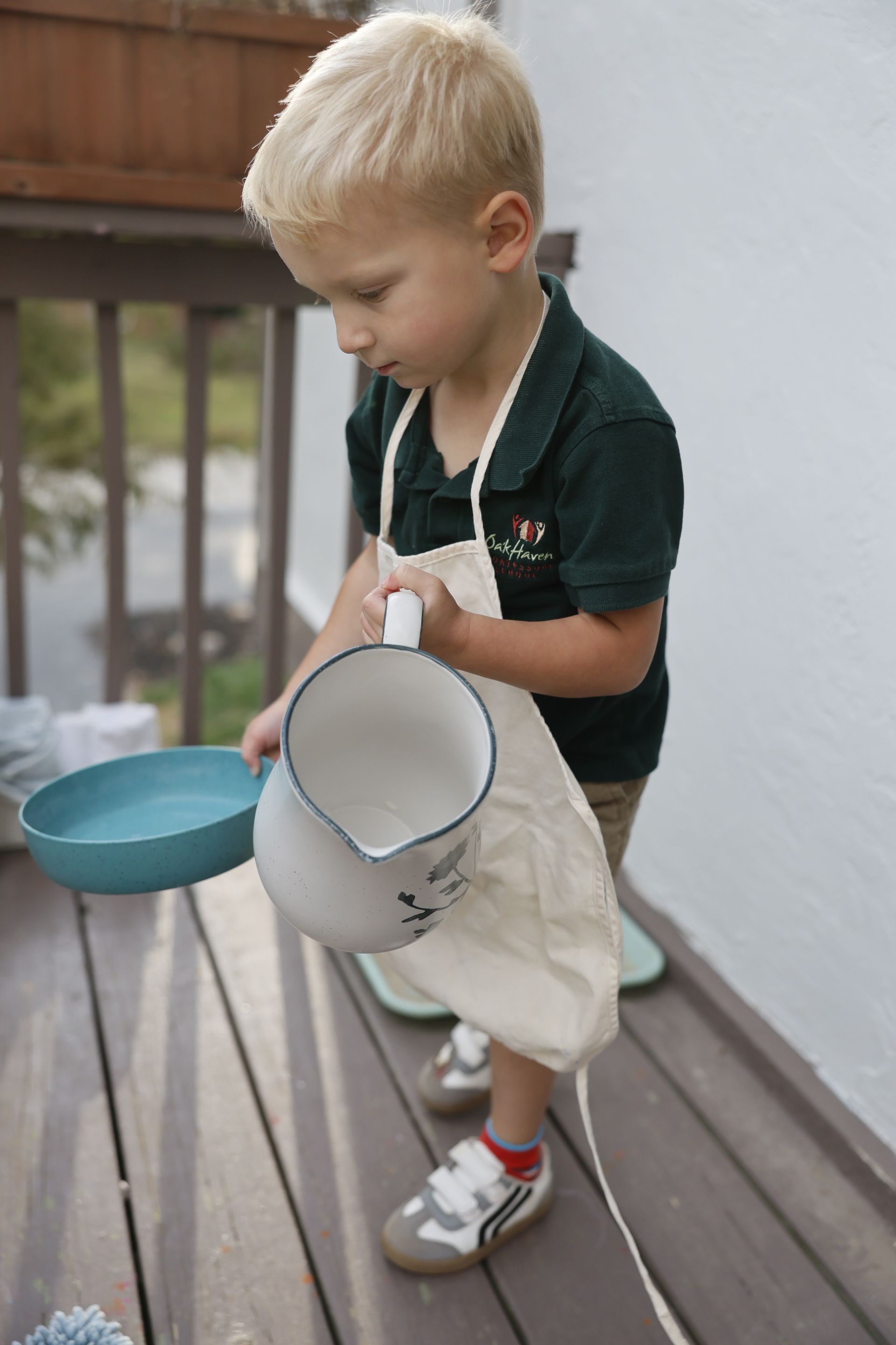 Child standing on a deck holding a white pail and blue bowl