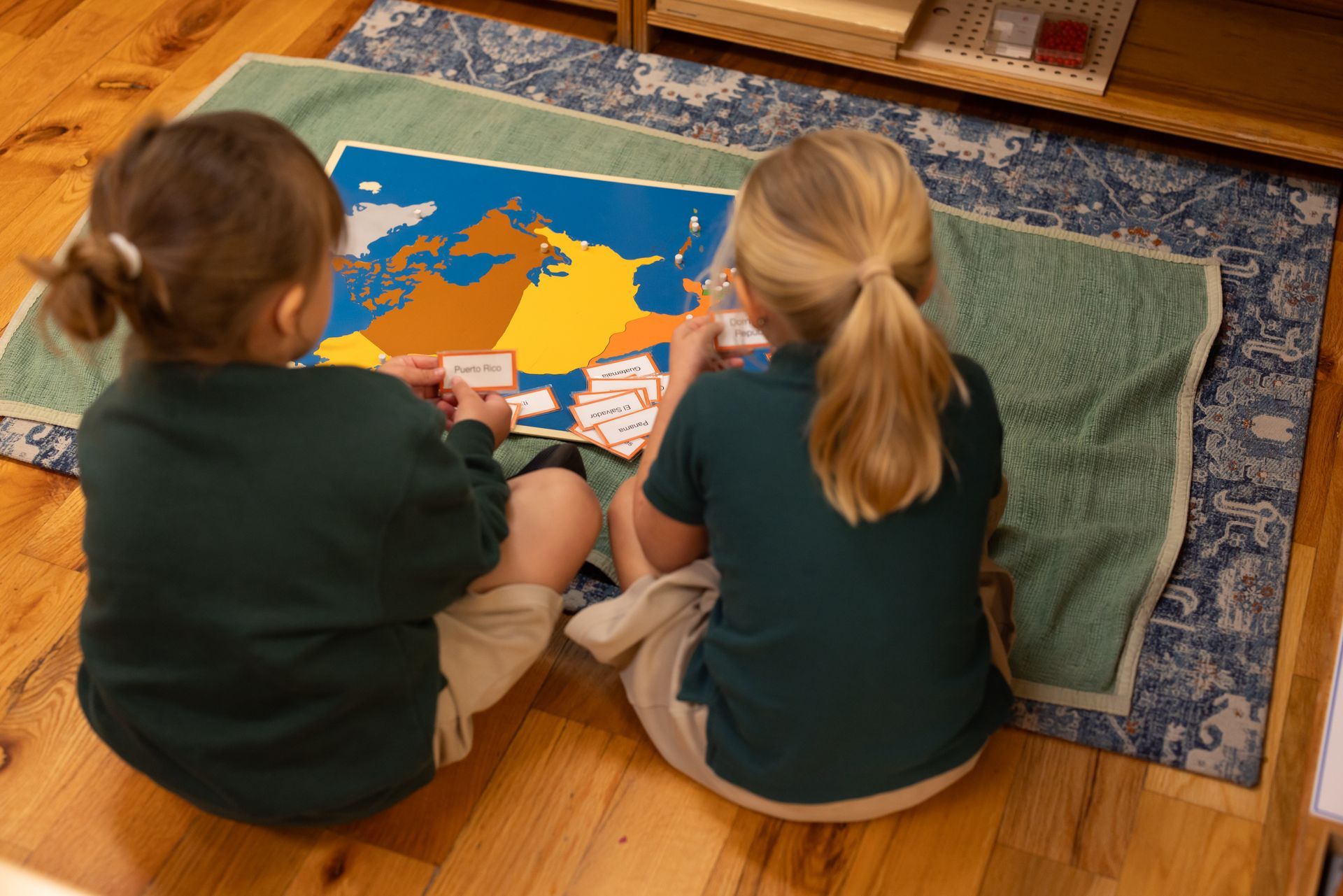 Two children sit on a rug playing with a colorful map puzzle.