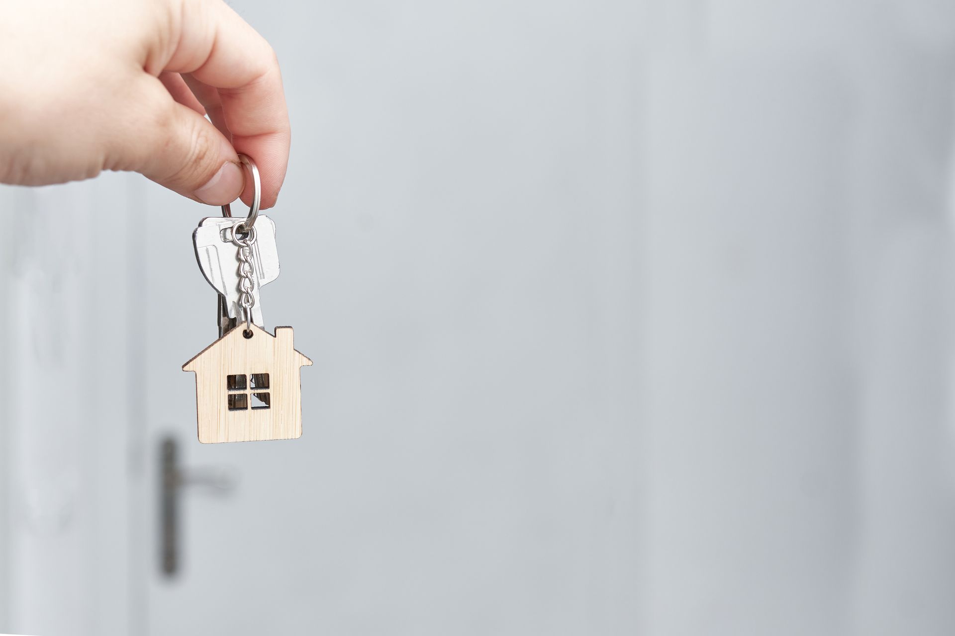 Hand holding a set of house keys with a small home-shaped keychain in front of a door.