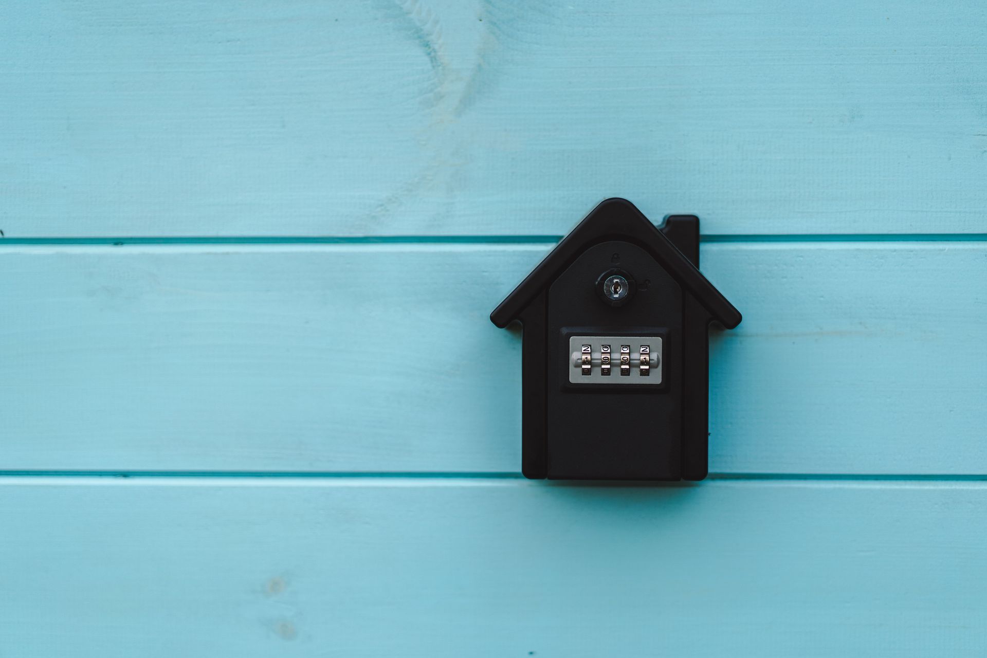 Combination lockbox mounted on a blue wooden wall for safe key storage at a property’s entrance.
