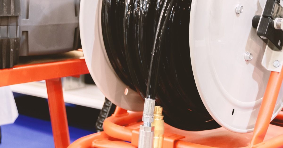 A black hose coiling around a reel with metal fittings and an orange stand beside an equipment case.