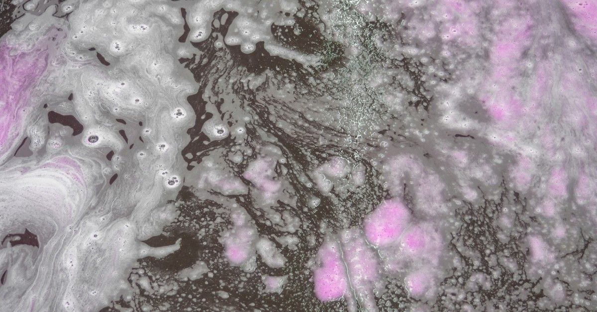 A combination of pink soap and white bubbles swirled together on the shower floor. The floor itself is quite dark.