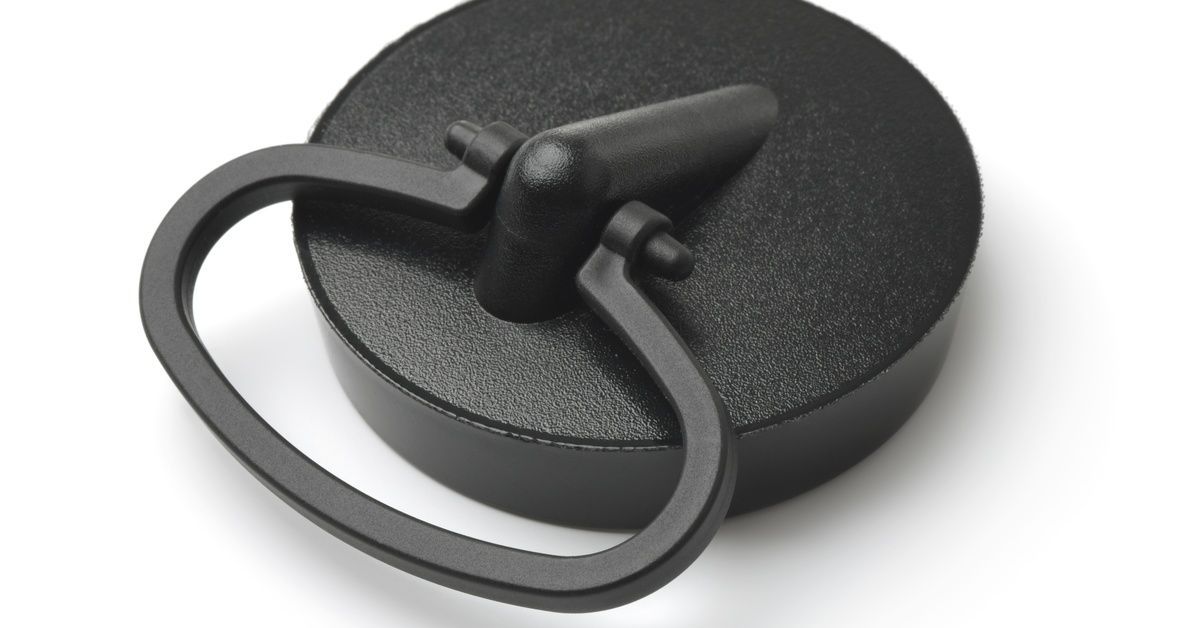 A black drain stopper. The stopper is made of plastic and has a loop handle for pulling it out of the drain.