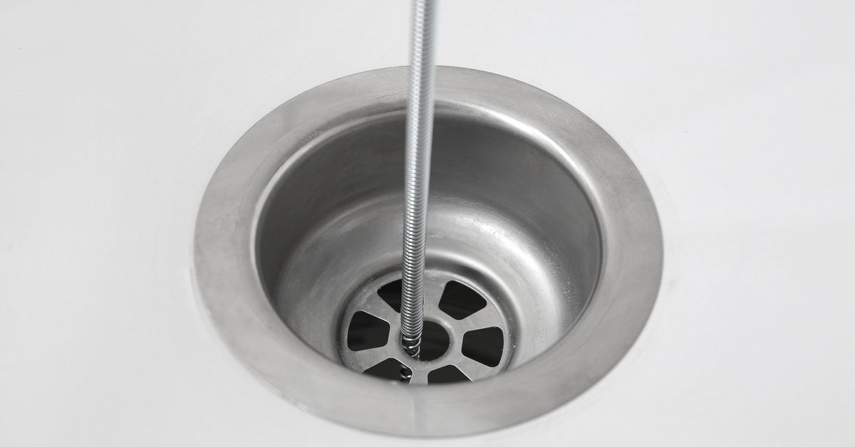 A plumber snake reaching down into the drain of a sink. It hasn't pulled anything out of the drain yet.