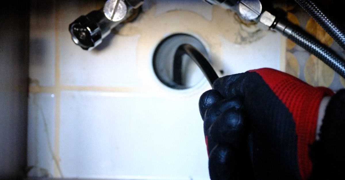 A plumber using a camera system to inspect and open a clogged bathroom drain during a sewer repair job.