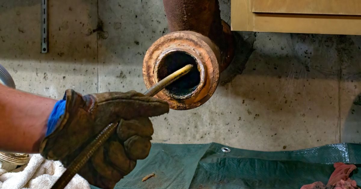 A plumber's hands run a camera scope through a main pipe to unclog a septic drain. The pipeline is quite rusty.