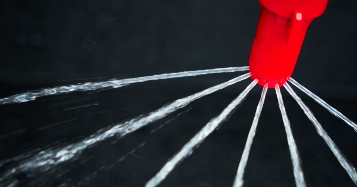 A red sprinkler nozzle spraying several streams of water in multiple directions in front of a dark background.