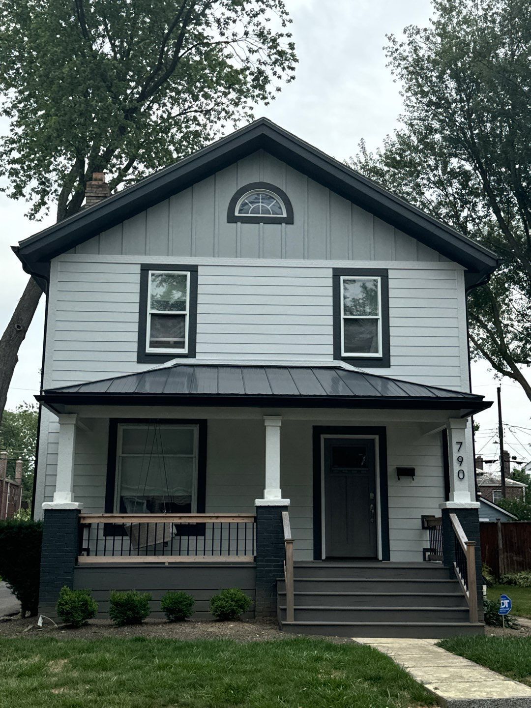 Two-story white house with black trim, front porch, and front steps under trees