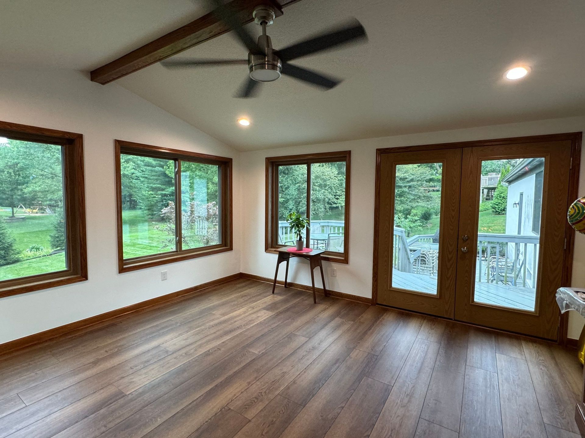 Empty sunroom with hardwood floors, large windows, ceiling fan, and French doors to a deck.