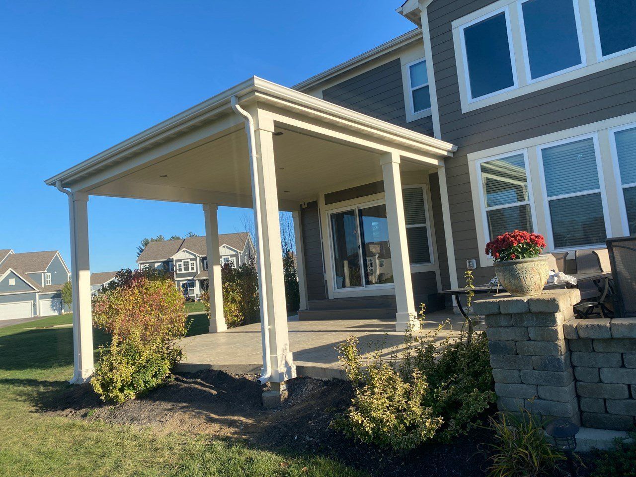 Covered front porch on a suburban house with white columns, stone steps, and potted red flowers.