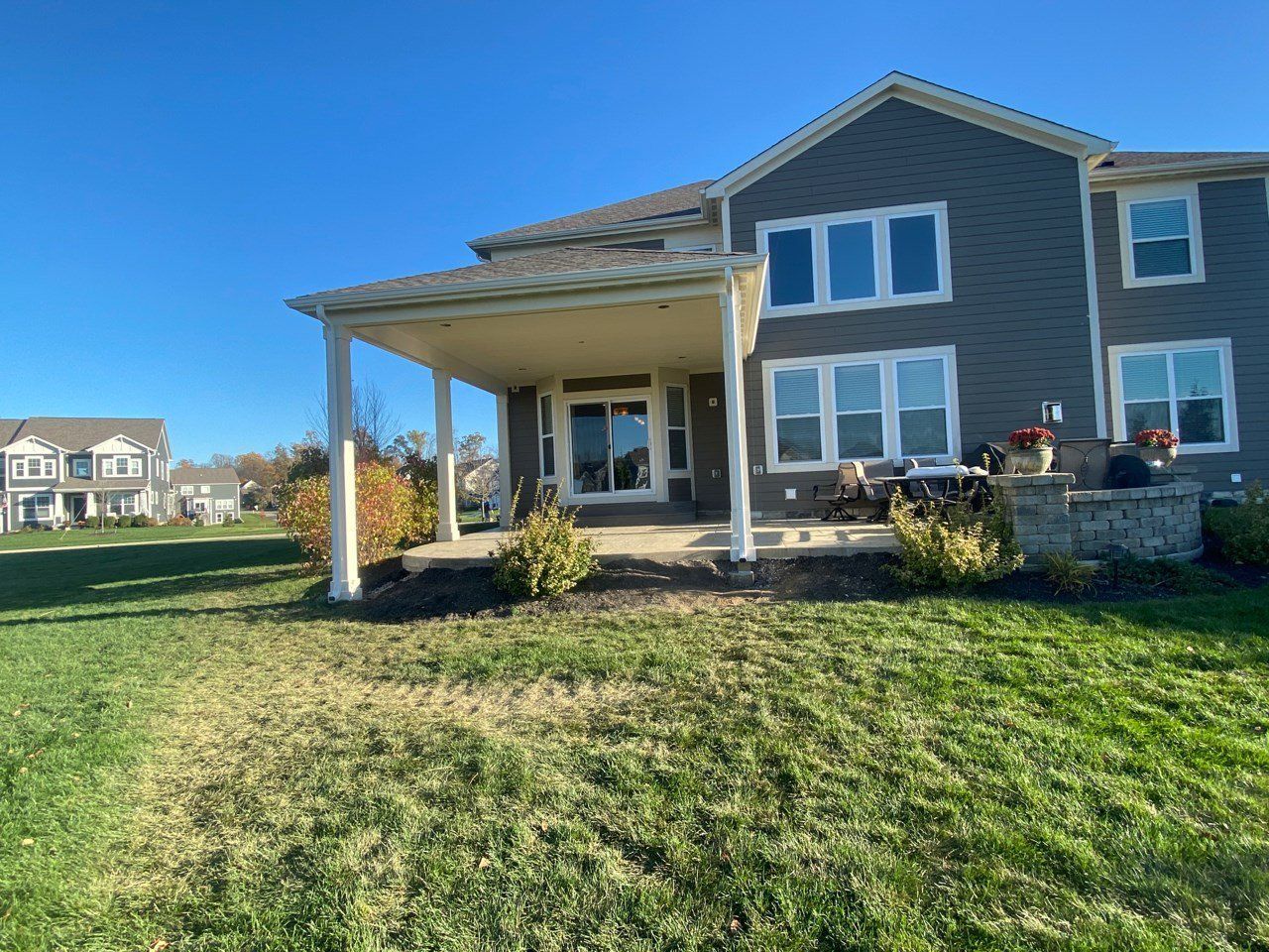 Blue two-story house with covered patio and large grassy yard under a clear sky