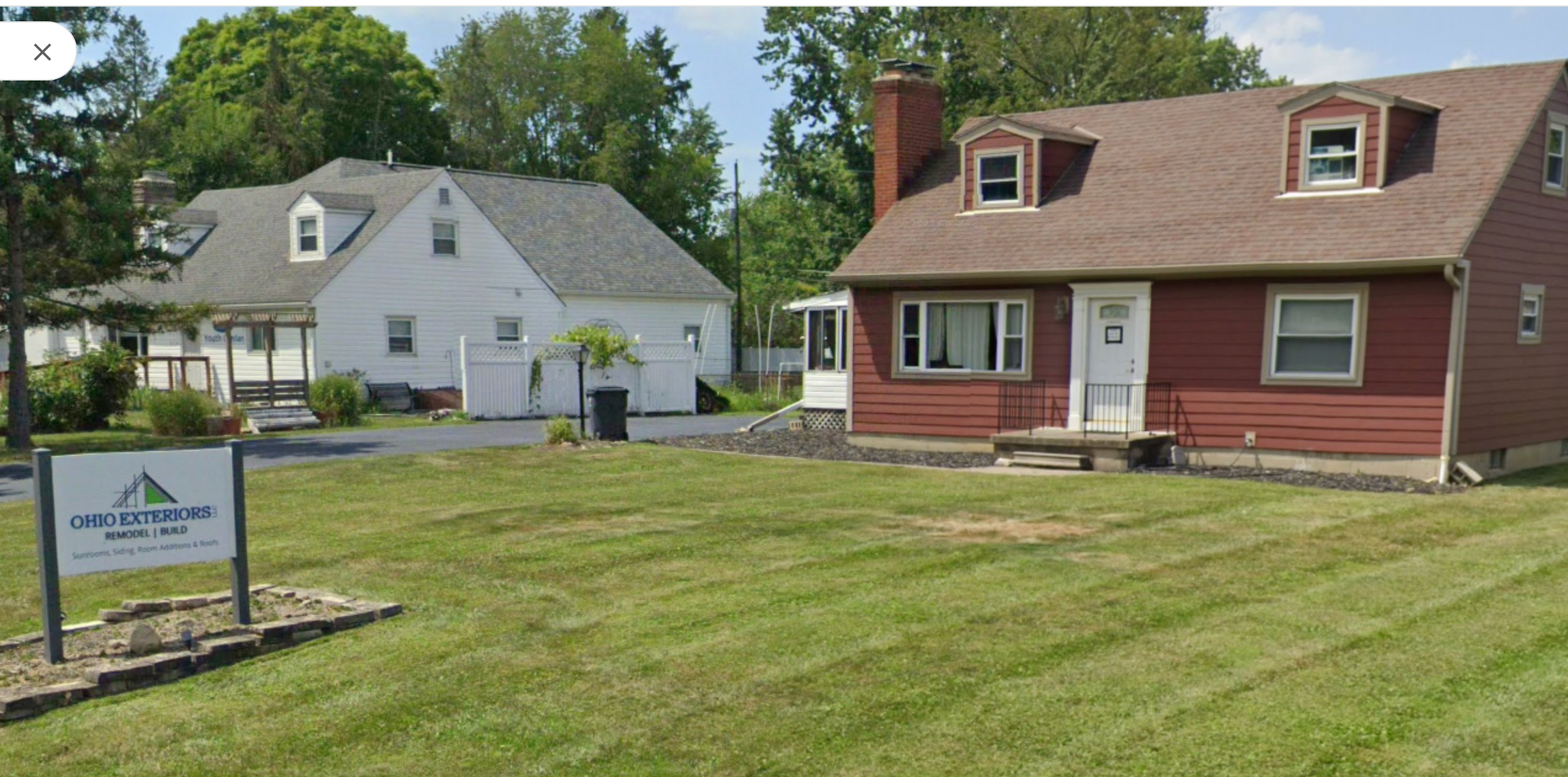 Suburban houses and a grassy lawn beside a real estate sign on a sunny day