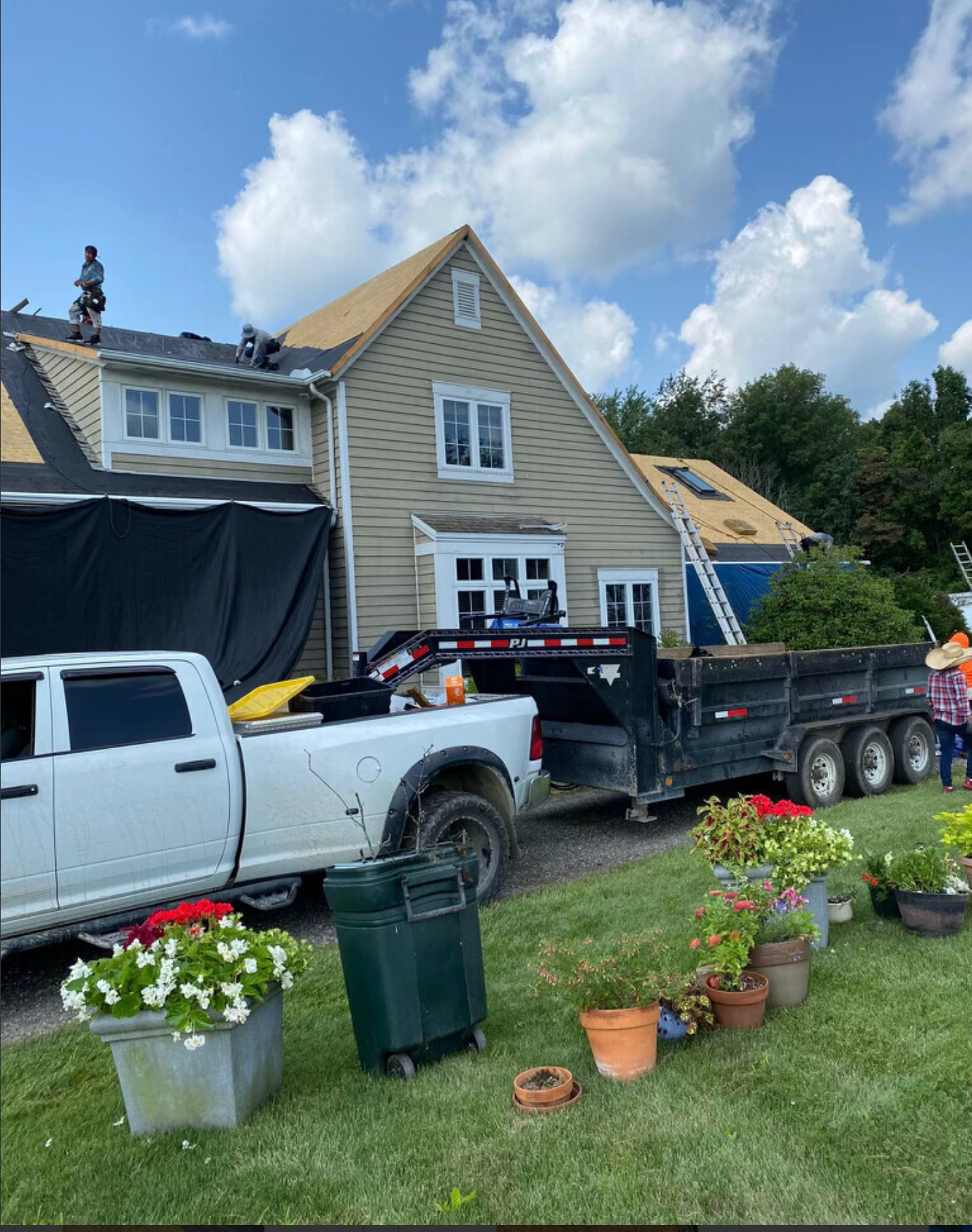 Two pickup trucks and a trailer parked outside a house with potted flowers on the lawn