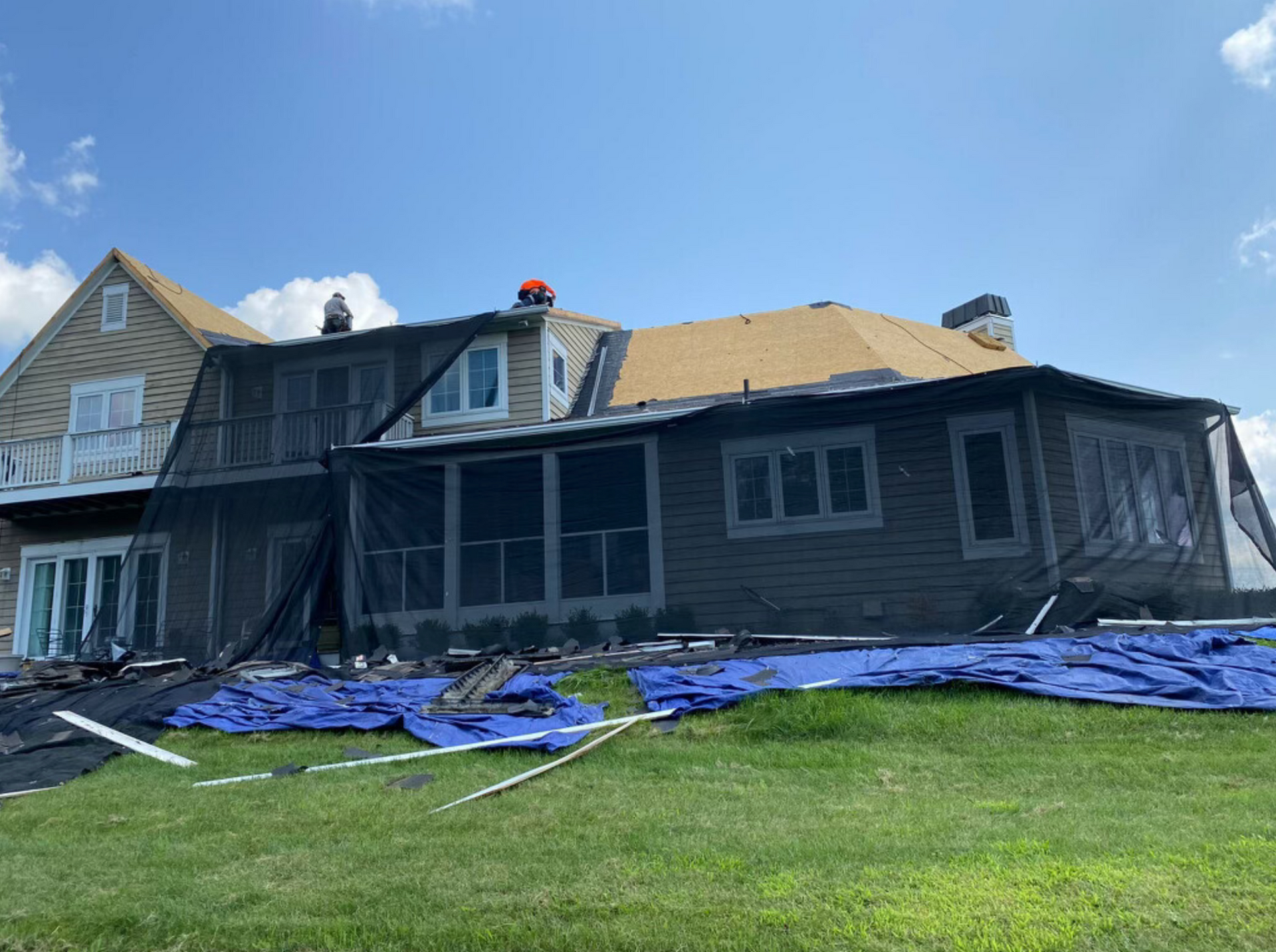 Damaged house with roof covered by tarps after storm, under blue sky