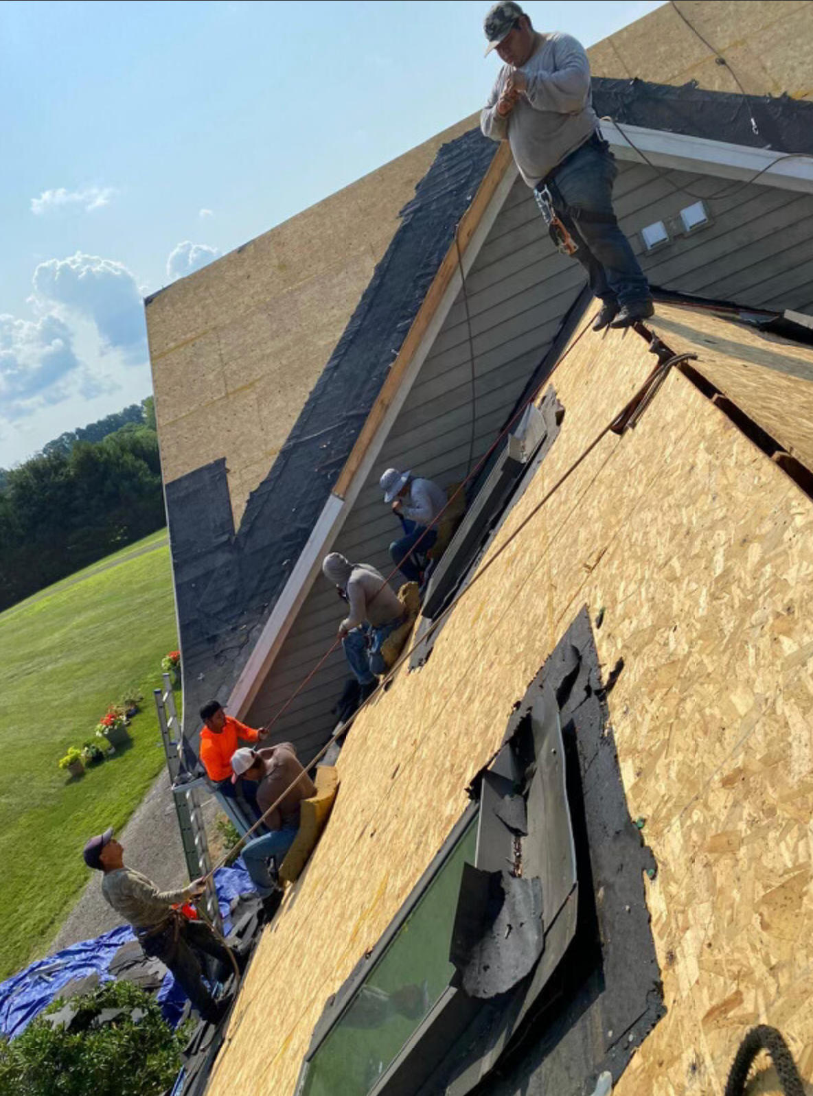 Workers installing shingles on a steep house roof, with one standing near the ridge and others below